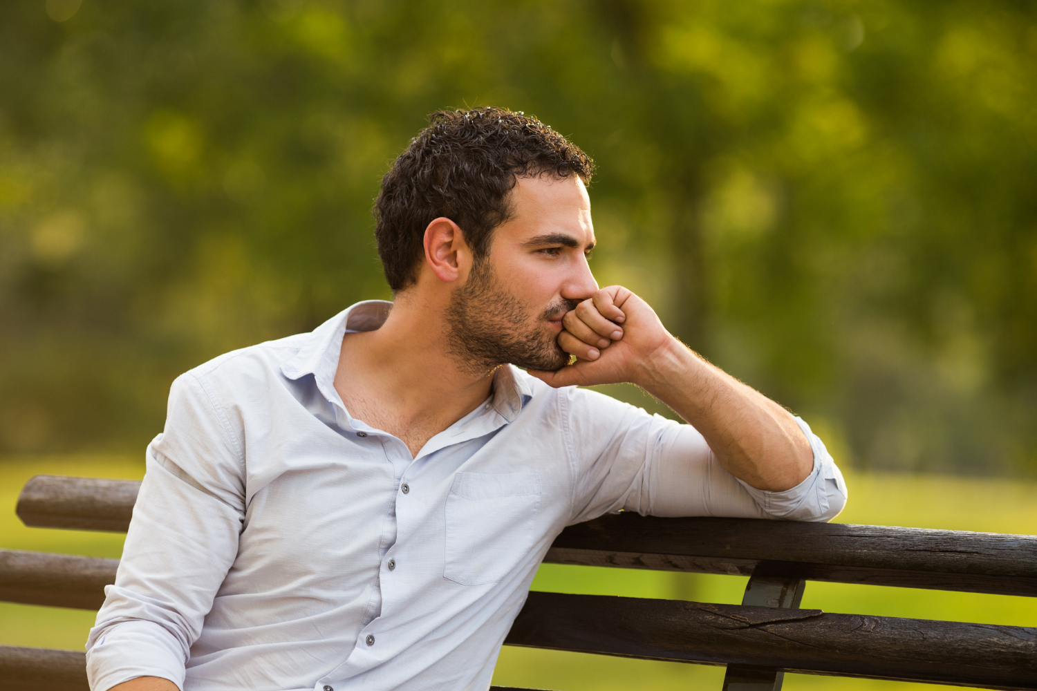 Outdoor park bench, man with short hair and beard, medium shot, daylight, editorial travel photo, one person.